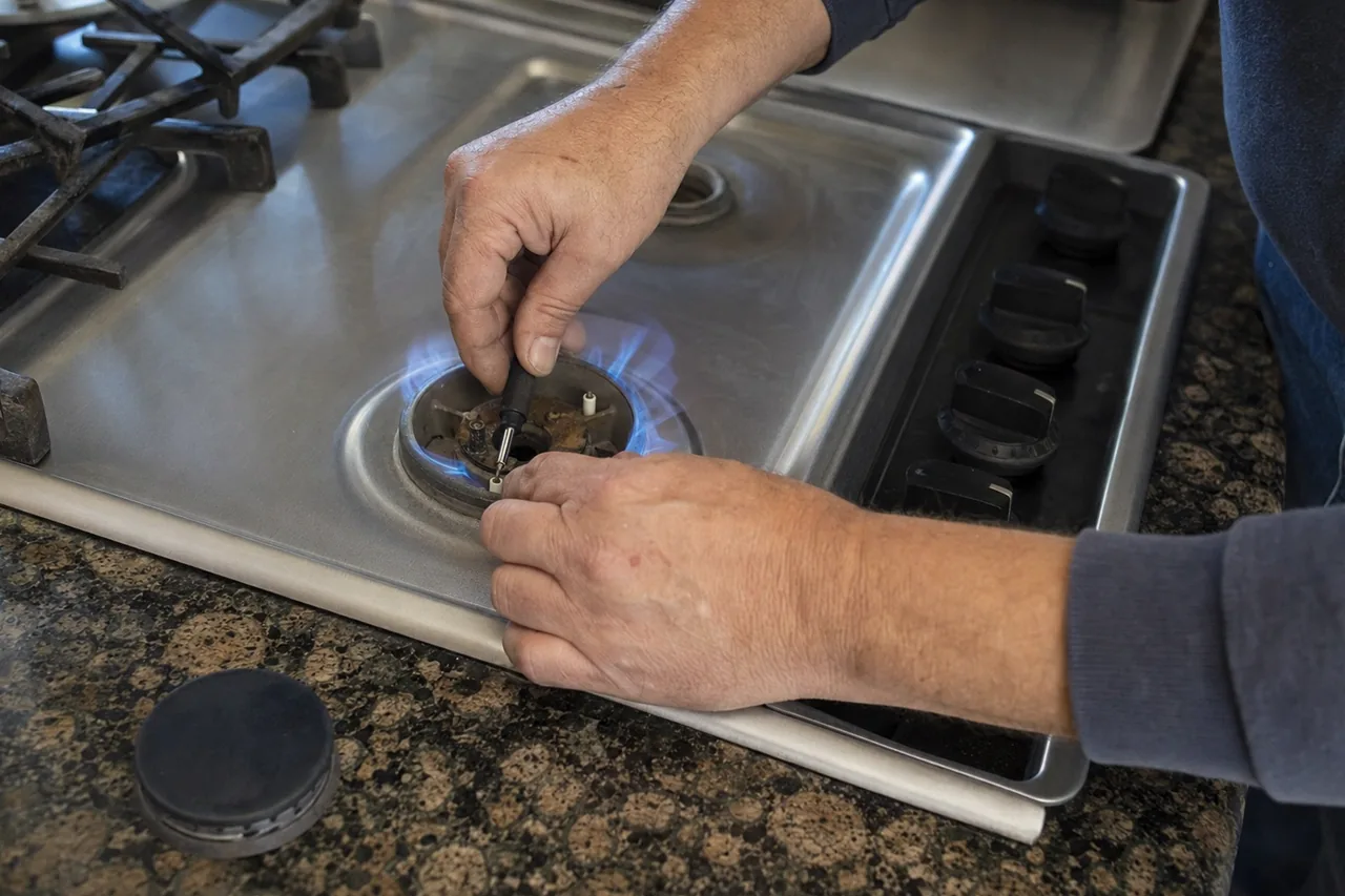 Close view of a pair of hands adjusting an igniter on a stainless gas cooktop set into a stone counter