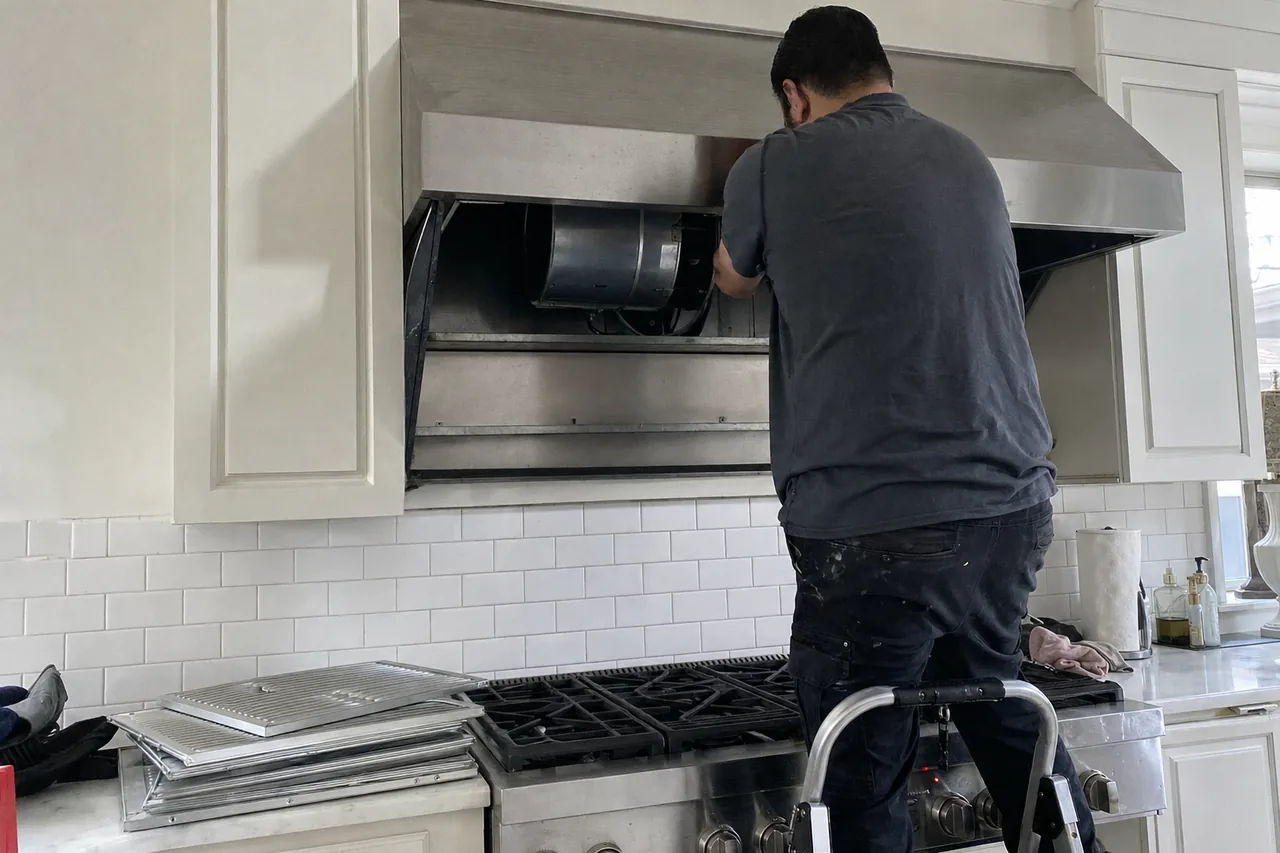 Technician on a step stool reaching into a stainless range hood with the baffle filters stacked on the counter below