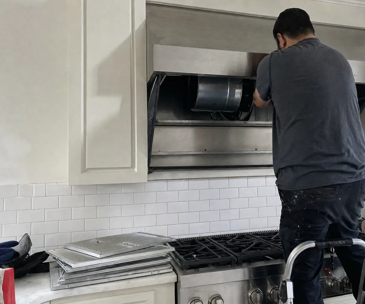 A step stool set on a kitchen floor below an open range hood with baffle filters resting on the worktop