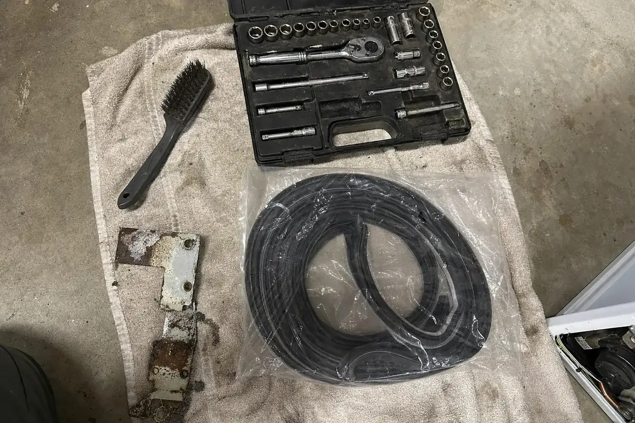 A wire brush and a socket set on a weathered towel next to a sealed replacement gasket in its bag