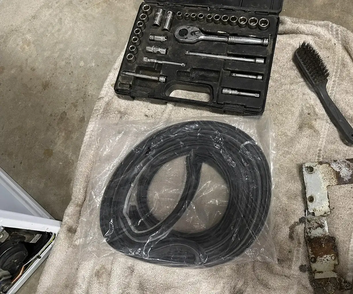 Overhead view of the left of a tool towel — a socket set and a wire brush on bare garage concrete