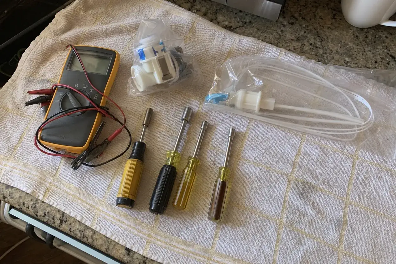 Overhead view of a working tool kit on a kitchen towel — a multimeter, nut drivers and bagged replacement parts