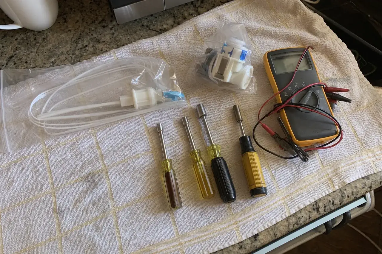 Replacement parts still sealed in their bags laid out beside nut drivers and a multimeter on a folded towel
