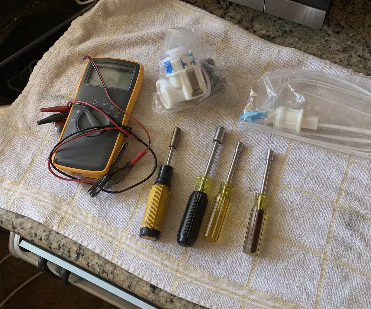 A multimeter, nut drivers and two bagged spares arranged on a kitchen towel, photographed from directly above